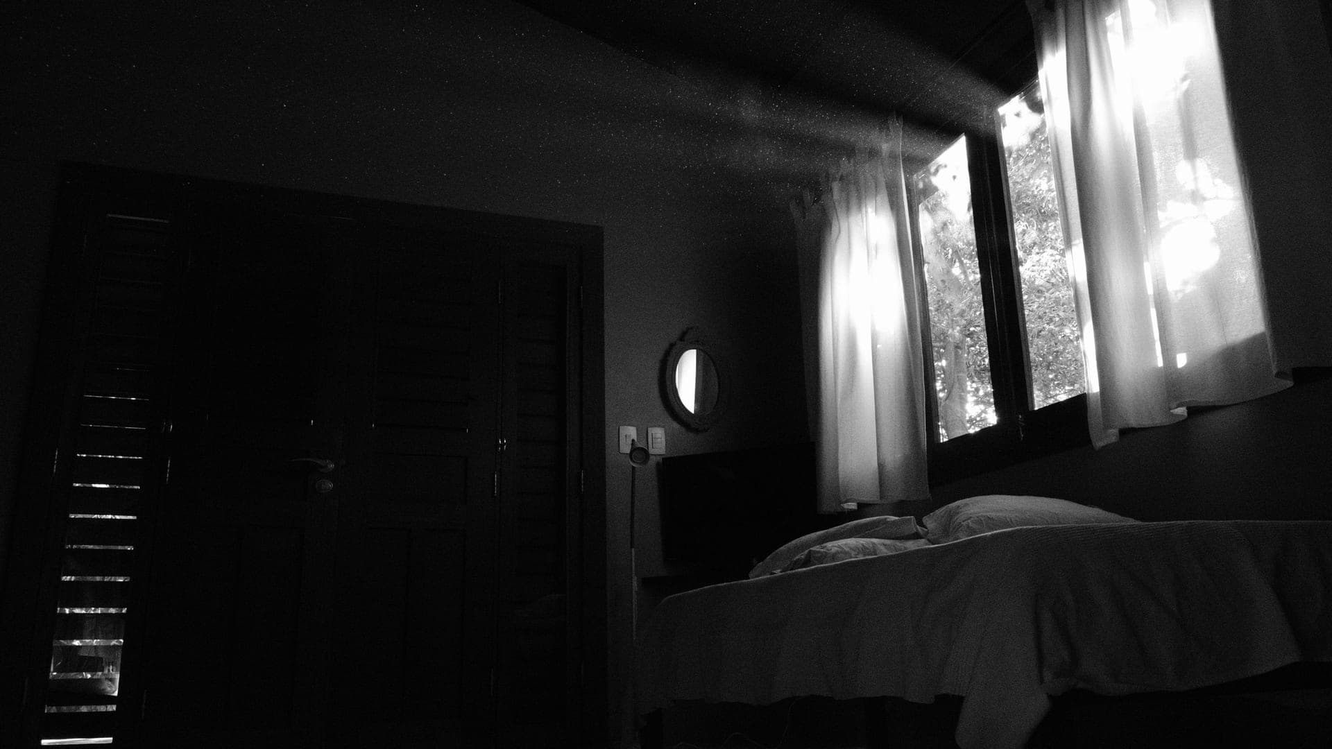 A dark bedroom at night with a closed door and a strip of light showing along the floor