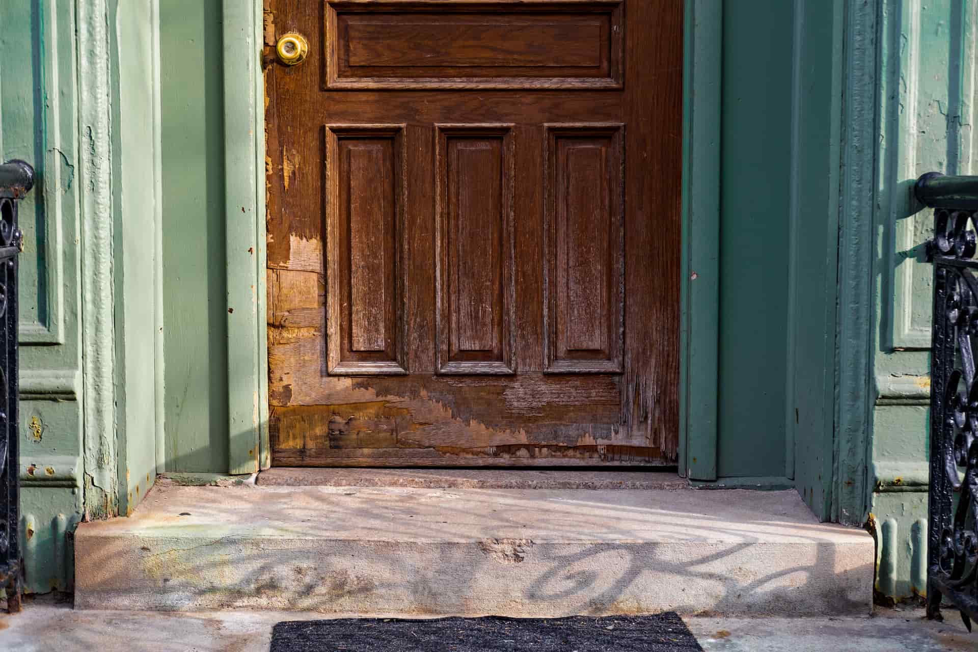 A close-up of an old wooden door with peeling paint and a worn frame