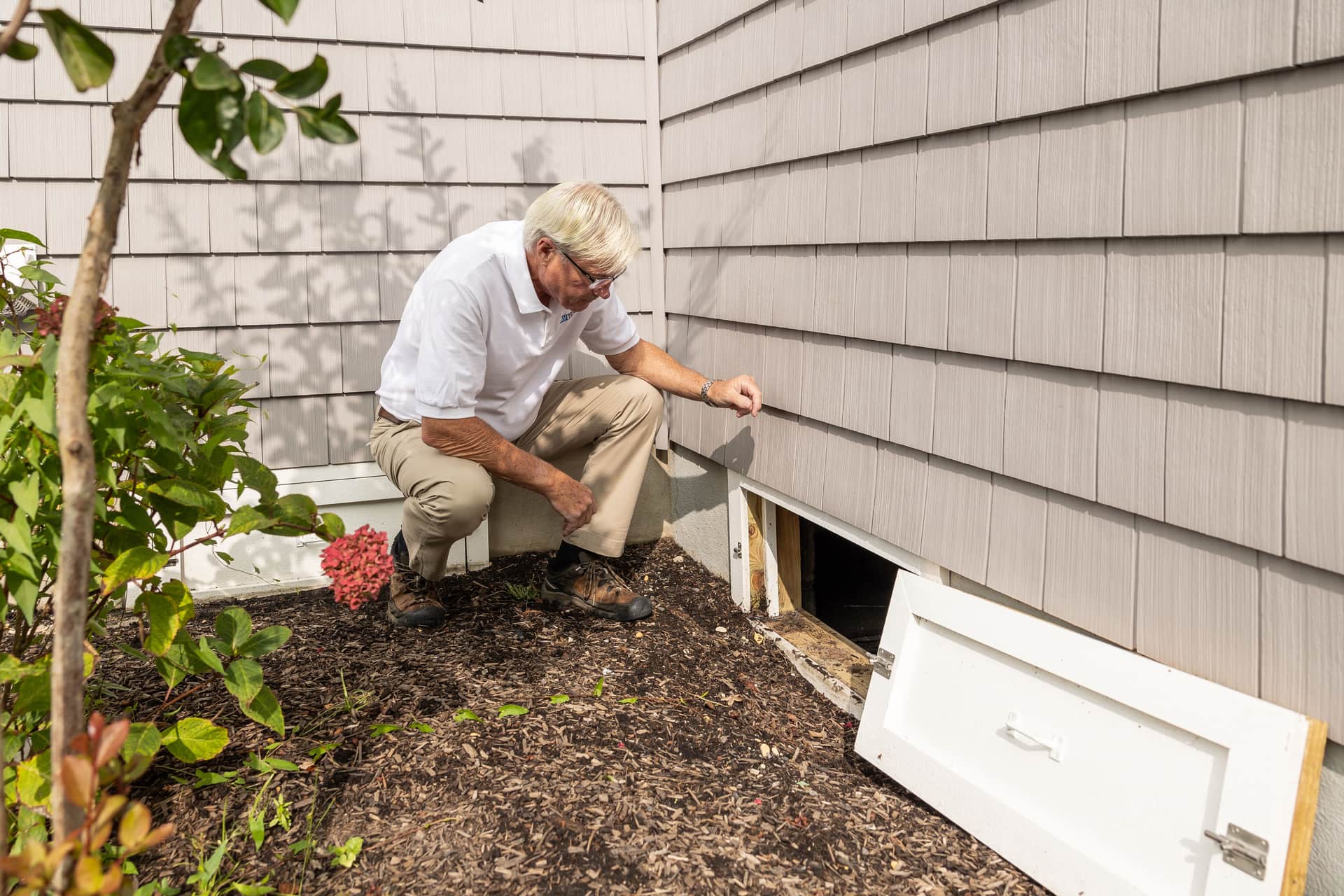 An inspector opening a crawl space access hatch in a house foundation