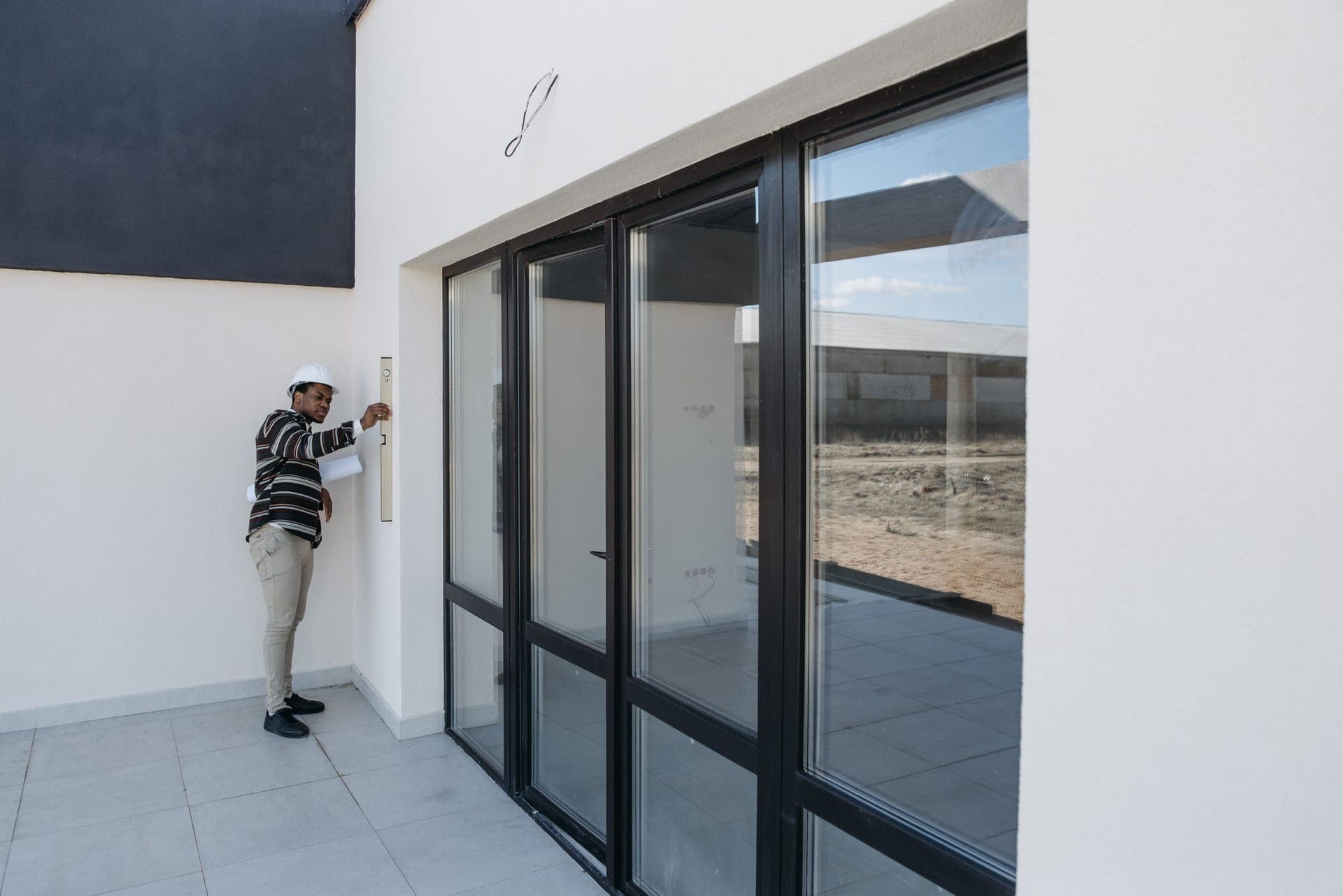 An inspector in a hard hat examining the wall and glazing of a house