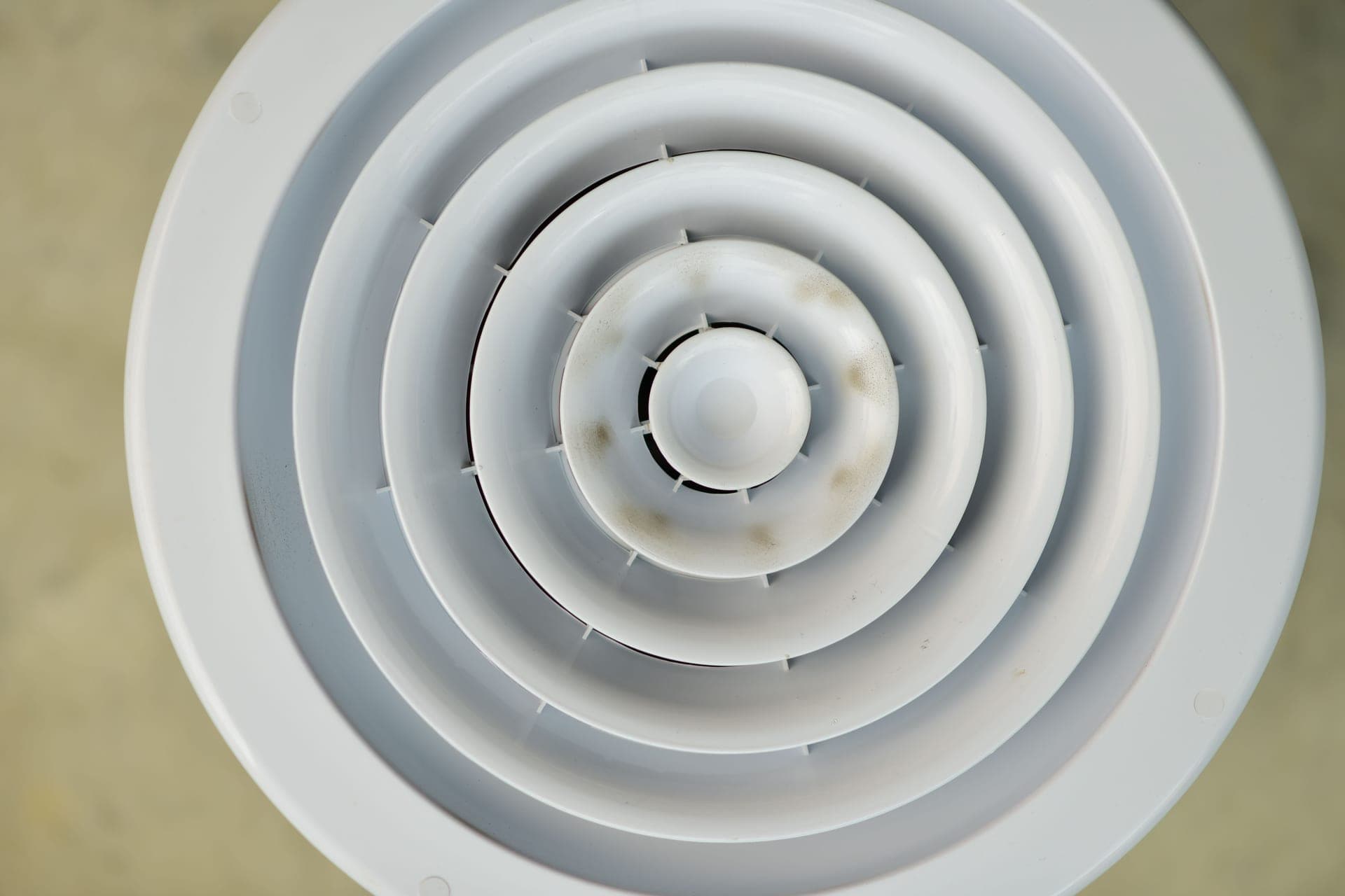 A circular metal air vent grille set into a wall