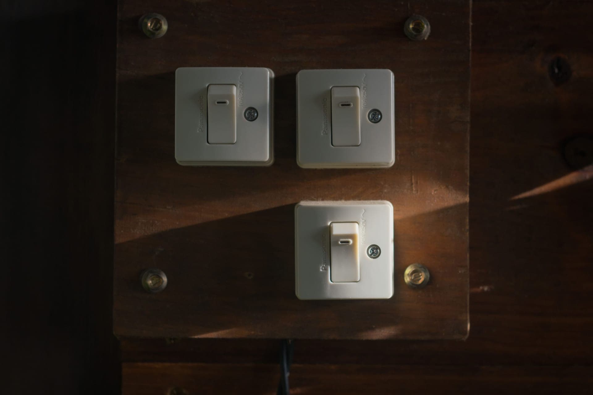 A light switch on an exterior wall with a hand held close to the plate to feel for moving air