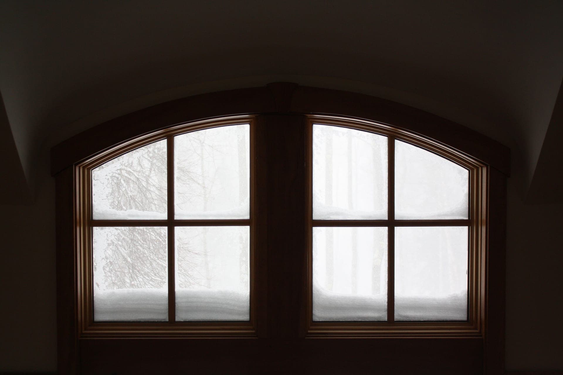 A stained wooden window with divided panes, snow banked against the glass outside