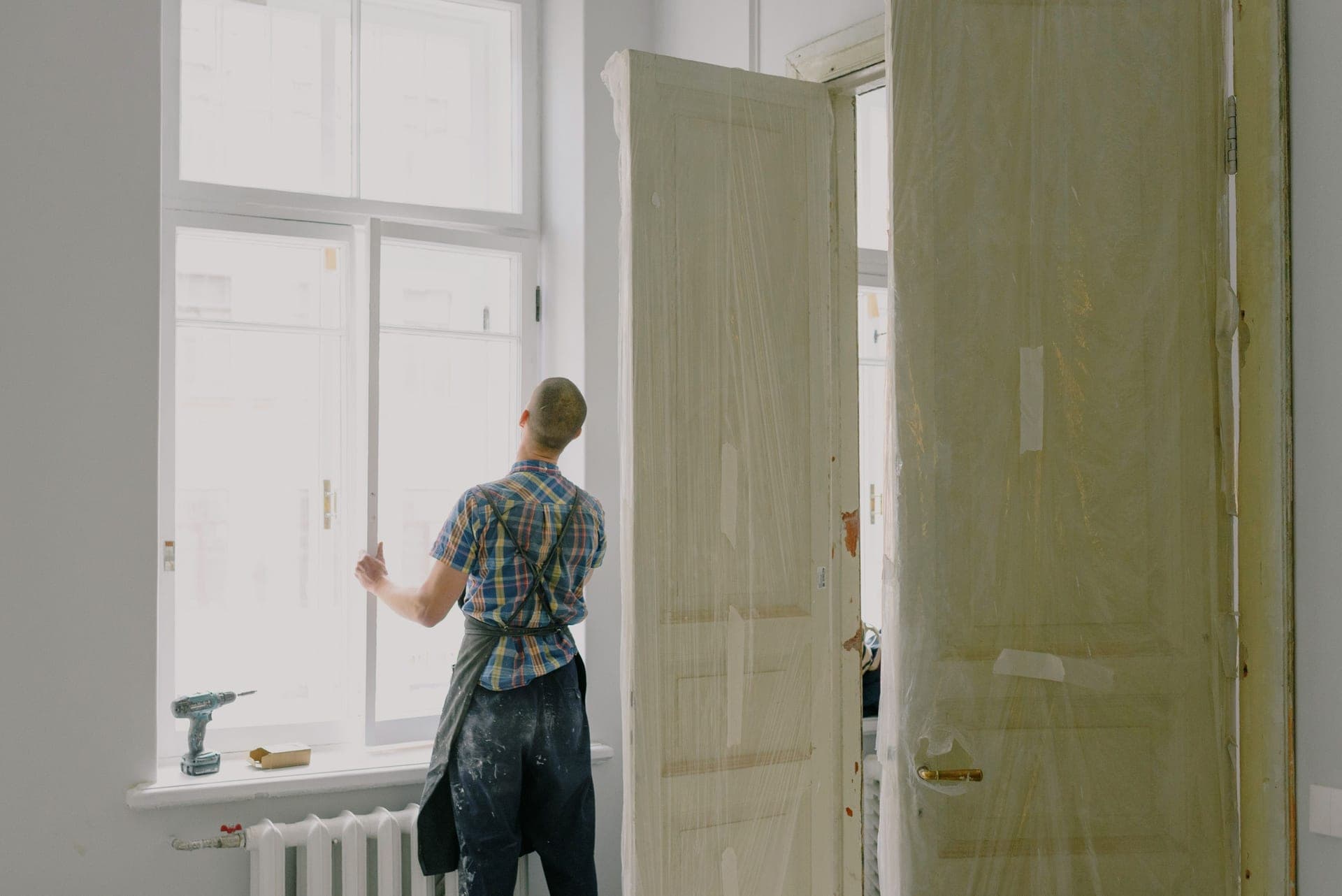 A hair dryer shrinking insulation film tight across an interior window frame in winter light