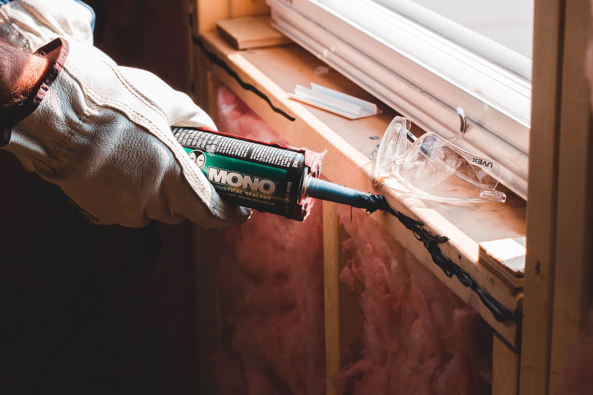 A hand pressing rope caulk into the joint between an old wooden window sash and its frame