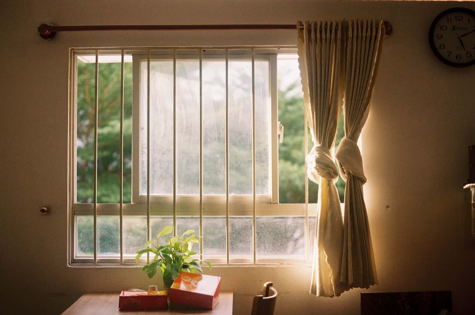 A heavy lined curtain drawn back from a bright, cold window with condensation on the lower pane